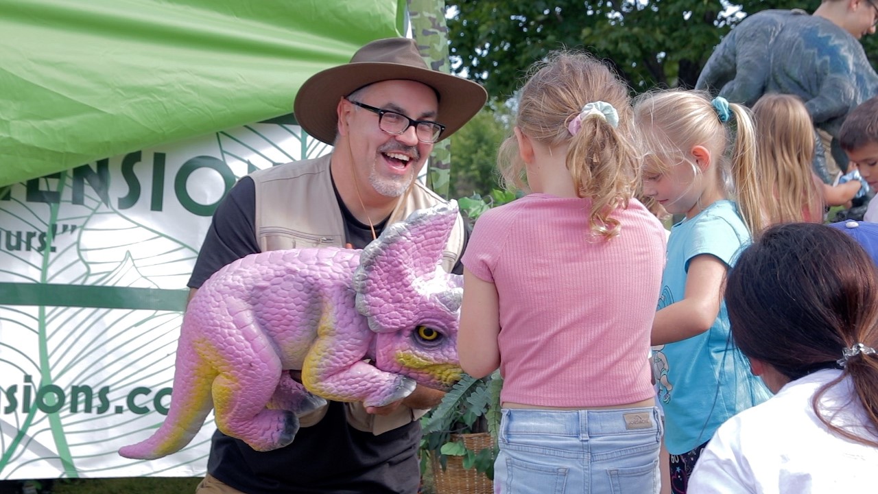 man holding pink baby stegasaurus out to children